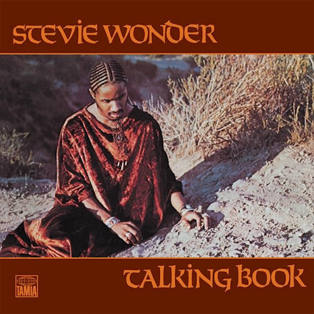 Album cover of "Talking Book" features a person sitting thoughtfully in desert terrain, wearing a flowing red patterned robe. The background shows dry plants and sand. The name "Stevie Wonder" and album title are in stylized orange text.