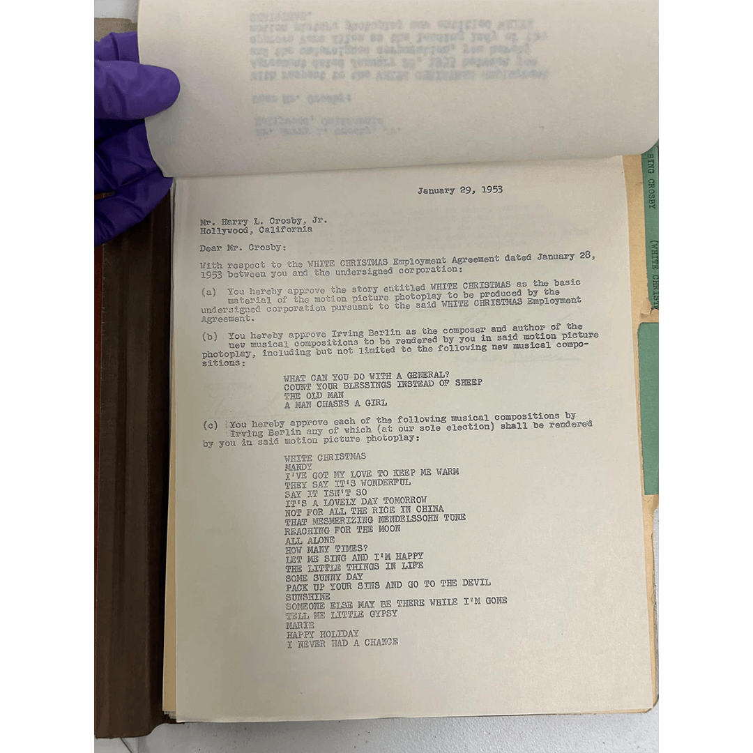 A typewritten page dated January 29, 1953, addressed to Mr. Harry L. Crosby Jr. It discusses an employment agreement related to "White Christmas," listing Irving Berlin's approved musical compositions. A purple-gloved hand holds the page, indicating careful handling.