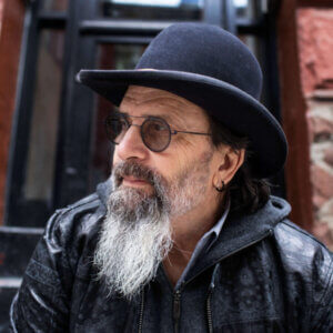 Portrait of Steve Earle in bowler hat and leather jacket, wearing glasses