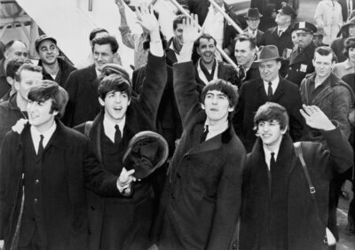 Black and White image of the Beatles getting off an airplane in America for the first time.